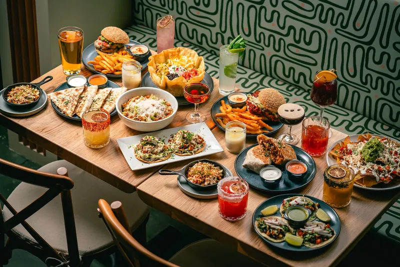 A selection of Mexican food dishes and cocktails spread across a booth table at Avenida