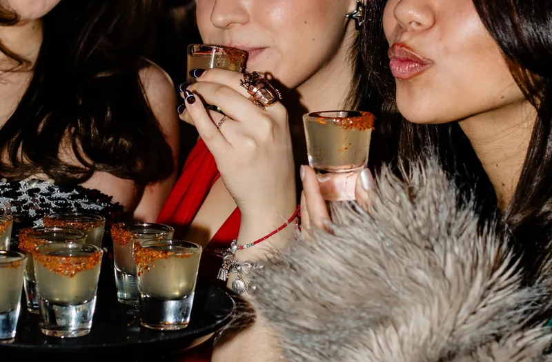 Three women drinking a tray of shots with Tajín rims at Avenida