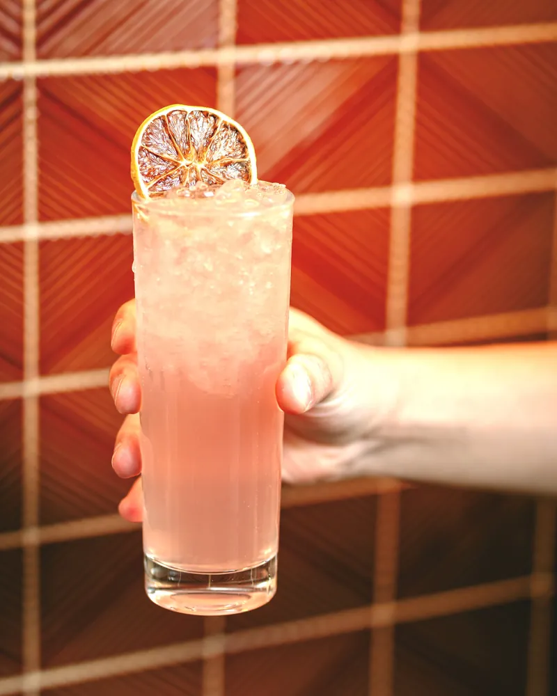A pink cocktail held in one hand in front of an orange and red wall